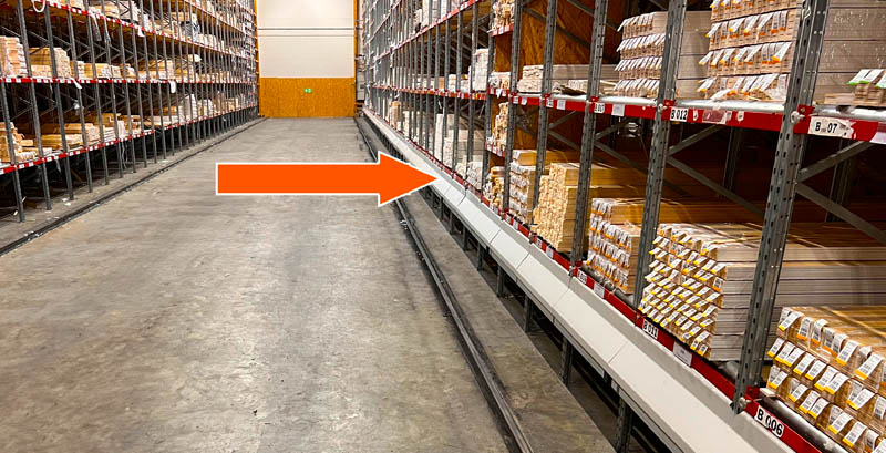 Warehouse floor with embedded rail track and cable channel; orange arrow highlights cable run along racking.