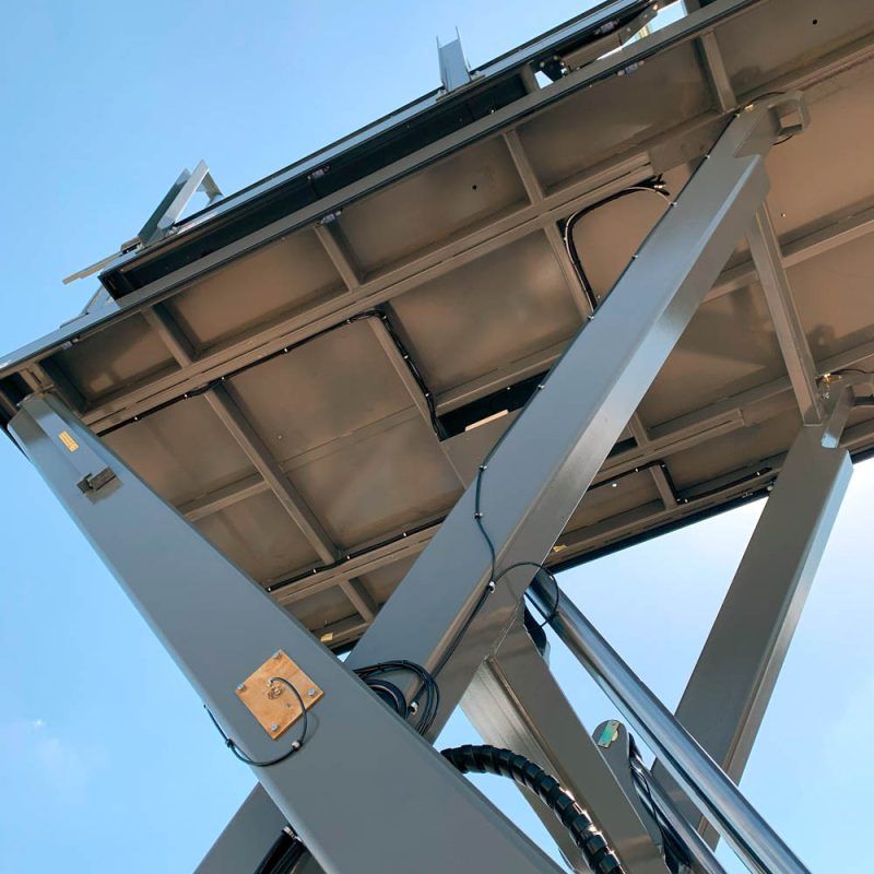 Low-angle close-up of hydraulic lift structure and cables under scissor lift platform.