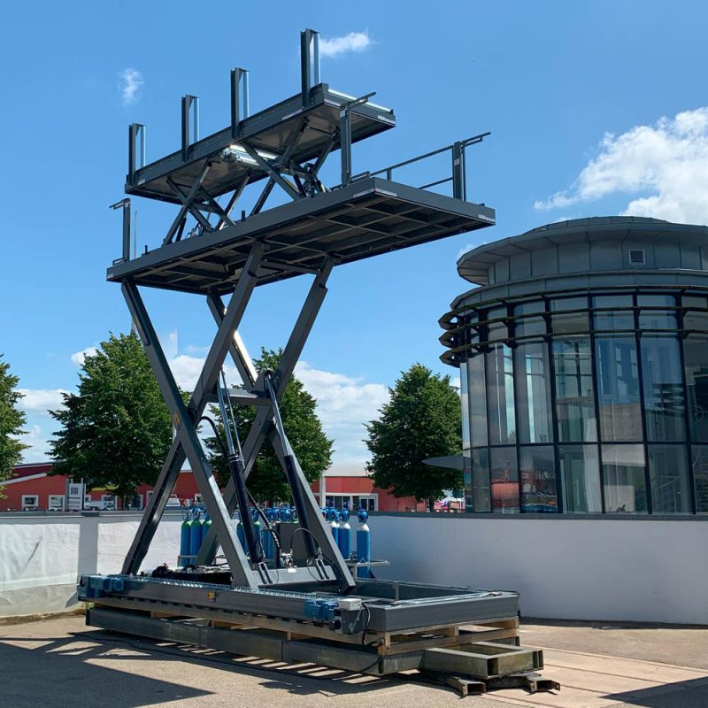 Railbound scissor lift platform fully extended in bright daylight with SIGI Europe office and blue sky in the background.