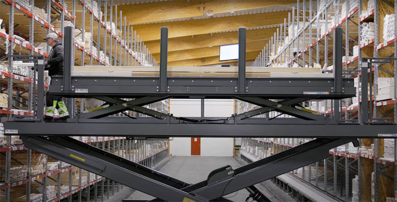 Warehouse worker using an elevated lift platform to pick materials from high storage shelves.